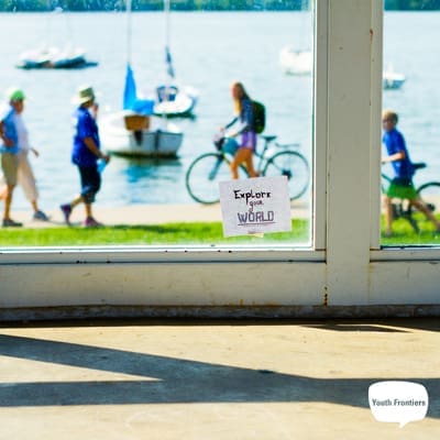 a post it note saying Explore Your World on a window overlooking a lake