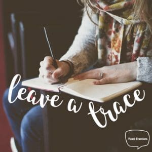 woman writing in a journal on a desk with a quote saying leave a trace