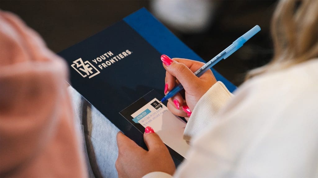 a youth frontiers navy folder with a female student writing an action card for character academy with a pen