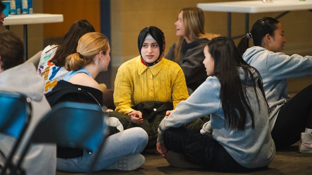 small group of students sitting together and having a conversation. the main student in the photo is a young woman in a yellow shirt and hijab