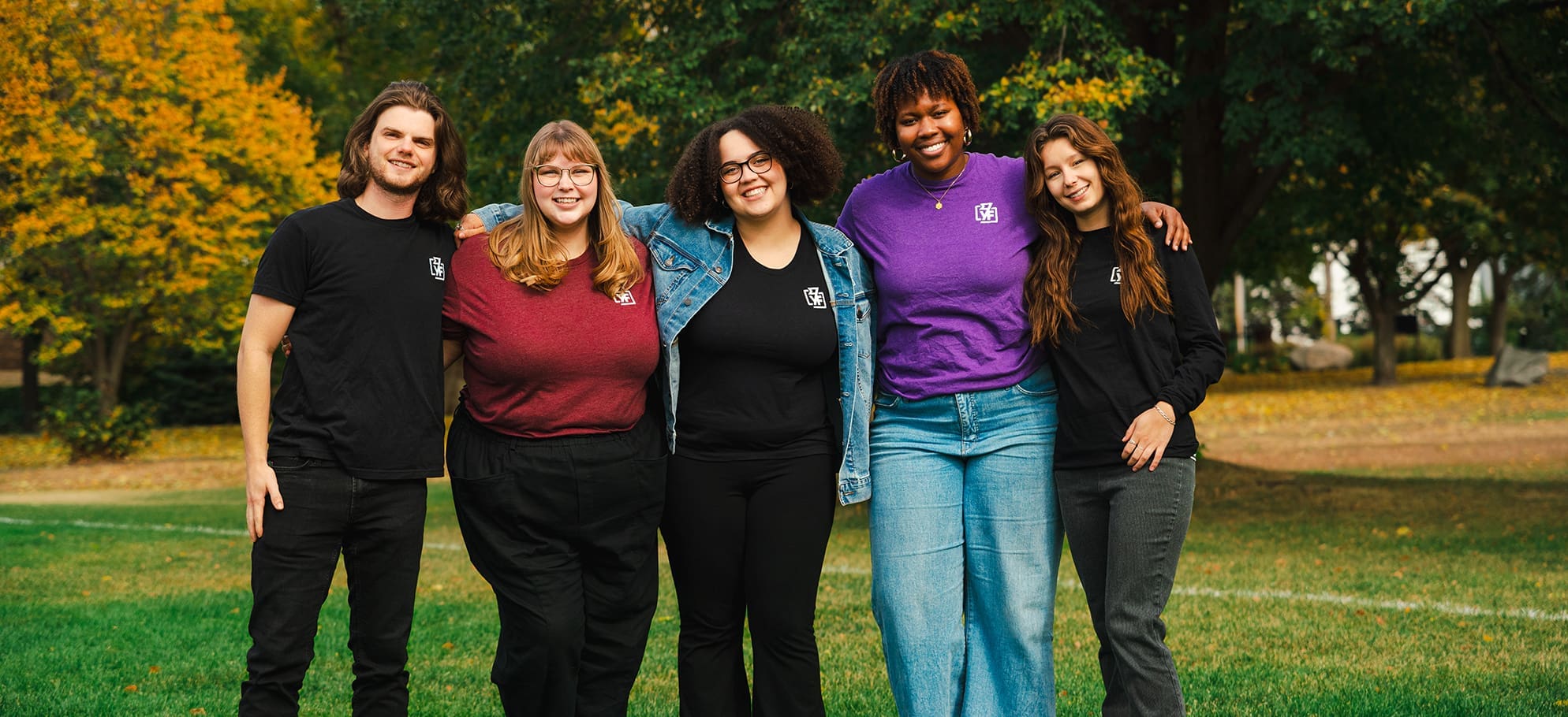 Y-Corps group photo of 5 post-college interns standing and smiling in a park with fall foliage behind them
